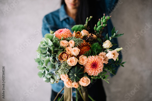 Very nice young woman holding big beautiful blossoming bouquet of fresh hydrangea, roses, cymbidium orchids, green trick carnations, green pumpkins, eustoma, nutan protea, dahlia, flowers photo