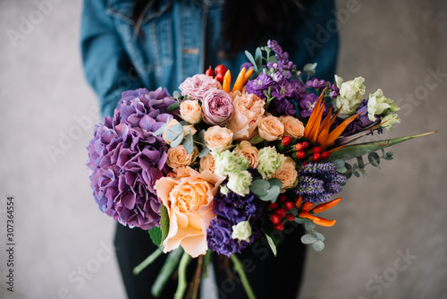 Very nice young woman holding big beautiful blossoming bouquet of fresh hydrangea, roses, campanella peach, eustoma, mattiola, oriental peppers, Strelitzia flowers in peach and purple colors photo