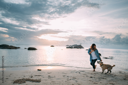 Girl has fun playing with a dog on the beach at sunset.