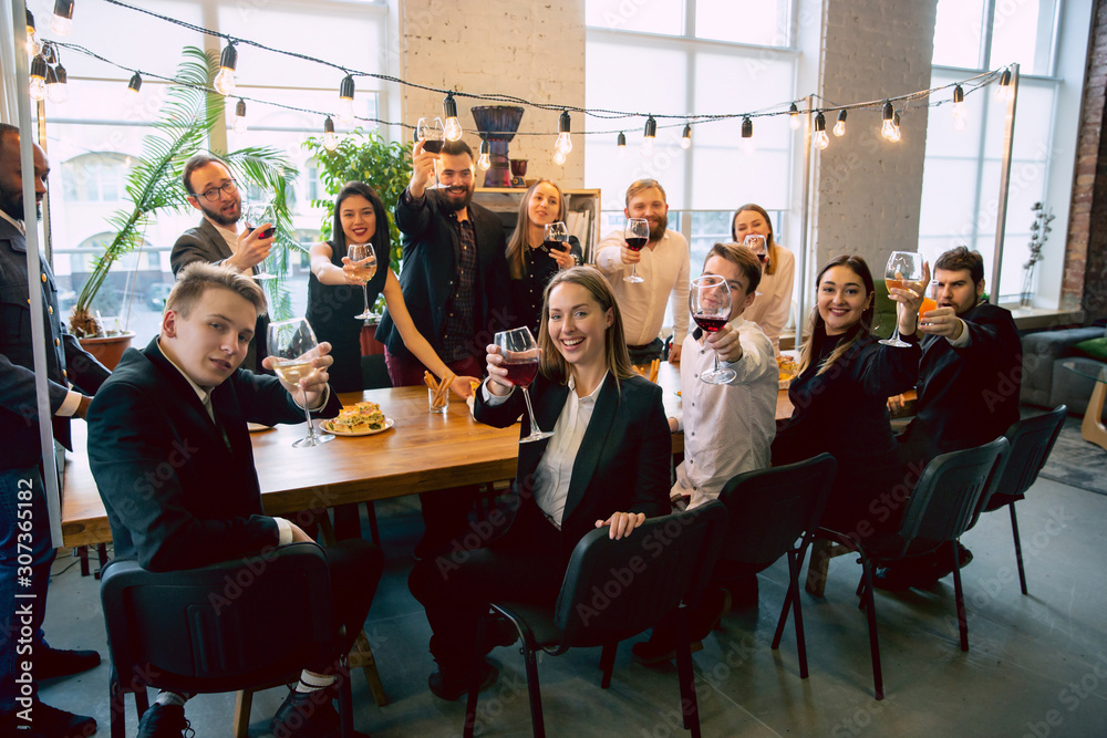 Happy co-workers celebrating while company party and corporate event. Young caucasian people in business attire cheering, laughting. Concept of office culture, teamwork, friendship, holidays, weekend. - obrazy, fototapety, plakaty 