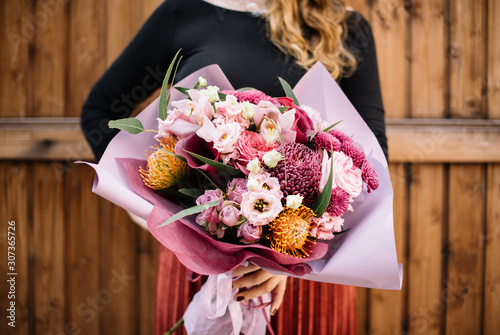 Very nice young woman holding big beautiful bouquet of fresh roses, carnations, eustoma, cymbidium, protea, chrysanthemum, eucalyptus, david austin roses flowers in colors pink and burgundy colors photo