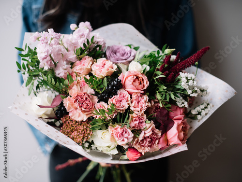 Fototapeta Naklejka Na Ścianę i Meble -  Very nice young woman holding big beautiful blossoming bouquet of fresh roses, carnations, matthiola, berries flowers in lavender and pink colors on the grey wall background