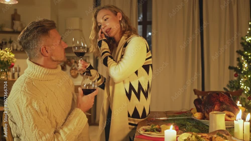 Pleased couple man and woman talking to each other about something while raising glasses and drinking wine at christmas time Pleased couple man and woman talking to each other about something while raising glasses and drinking wine at christmas time