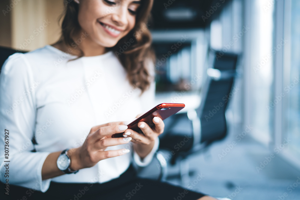 Cheerful young beautiful woman in formal outfit sitting surfing smartphone in workplace Cheerful young beautiful woman in formal outfit sitting surfing smartphone in workplace