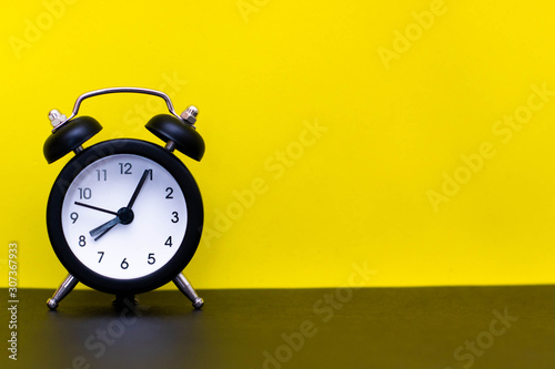 Black alarm clock on a yellow background. Place for text, copy space.