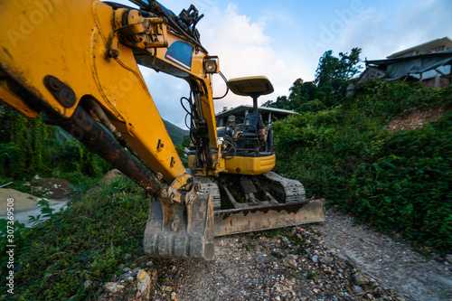 The modern excavator on the construction site with sunset sky. Large tracked excavator standing on a hill with a green grass. Machinery for a construction of a new building in the countryside.