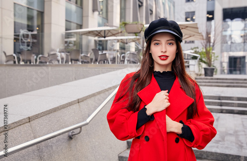 фотографія Lovely charming ravishing calm girl in black kepi holds her overcoat by hands ne