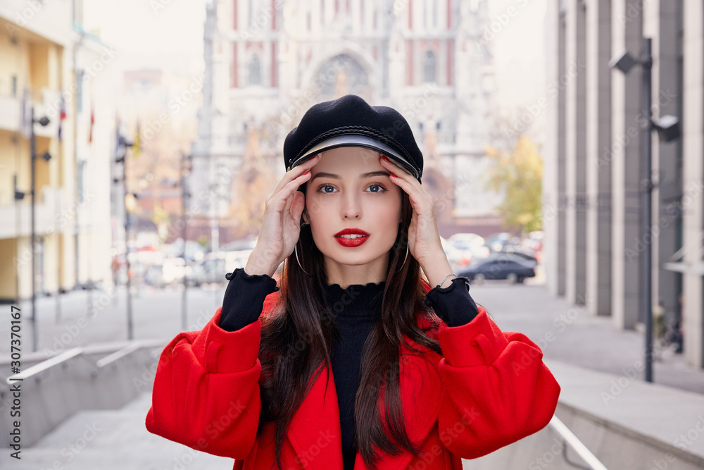 Stunning charming unsurpassed girl with bright red lips looks directly and holds hands near temples Stunning charming unsurpassed girl with bright red lips looks directly and holds hands near temples