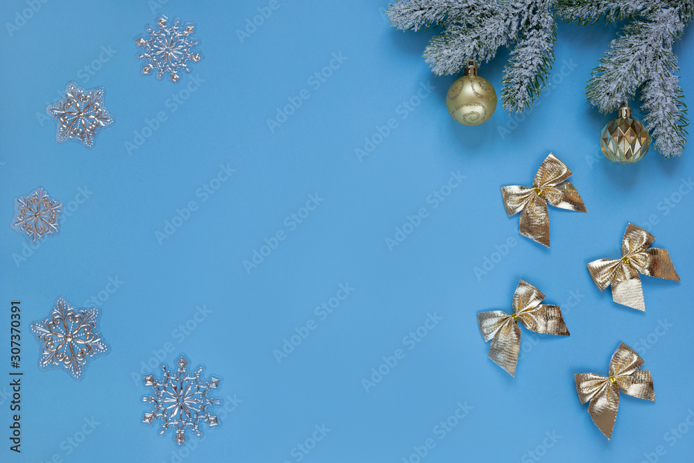 Naklejka premium Snowy sprig of pine with christmas balls, snowflakes and gold christmas bow ties isolated on blue background. Flat lay.