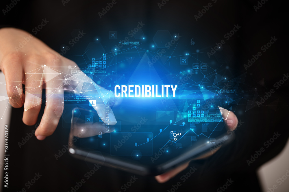 Businessman holding a foldable smartphone with CREDIBILITY inscription, business concept Businessman holding a foldable smartphone with CREDIBILITY inscription, business concept