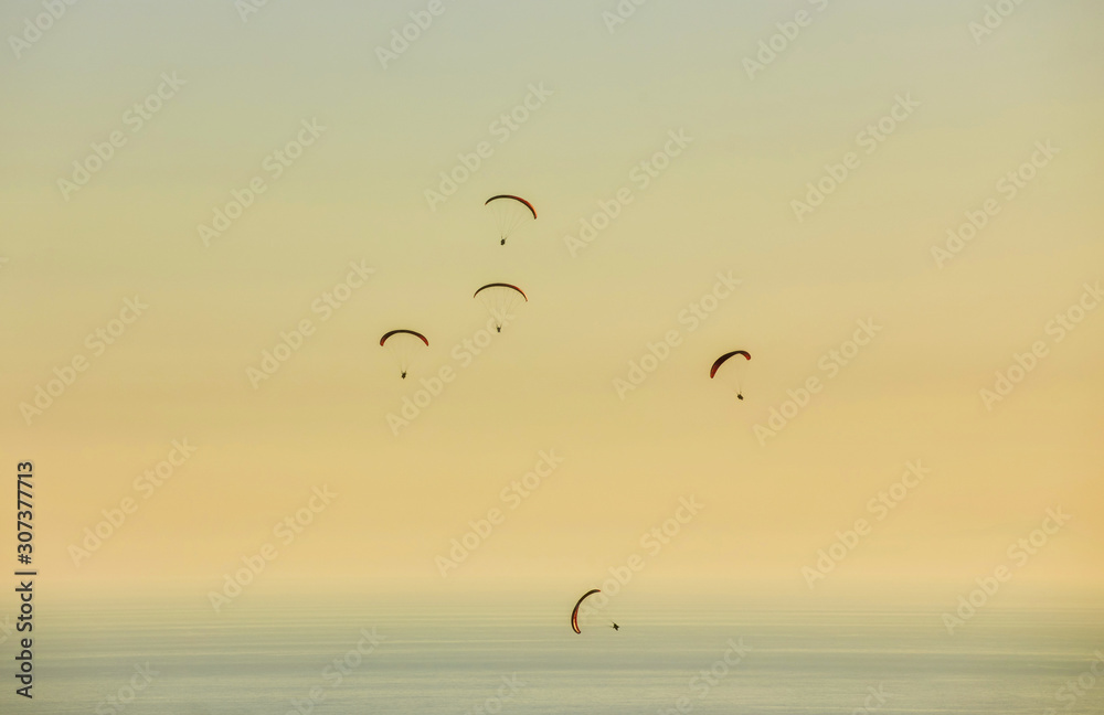 Silhouette of powered paraglider soaring flight over the sea against marvellous orange sunset sky.
