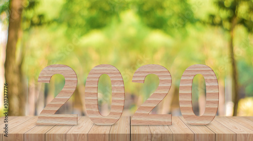 Happy new year 2020 wooden number on wood table with sunlight and green bokeh background.