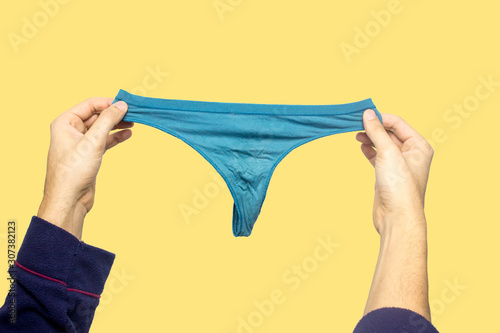 Man holding a tanga. Aqua menthe color, yellow background. Concept of lingerie, man wants become a female or the opposite, lgbt, transgender. Man who can't understand difference between female panties