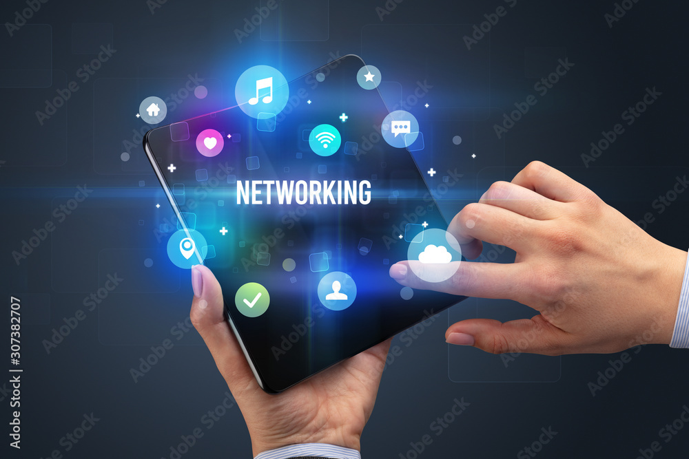 Businessman holding a foldable smartphone with NETWORKING inscription, social media concept Businessman holding a foldable smartphone with NETWORKING inscription, social media concept
