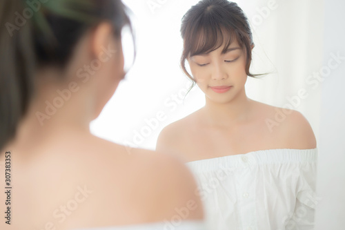 Beauty portrait young asian woman smiling look at mirror of checking skin care caucasian with wellness in the bedroom  beautiful girl happy touching face in reflection for health  lifestyle concept.