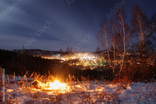 Night fire on the mountain on the background of the bright sunset town village under a dark sky
