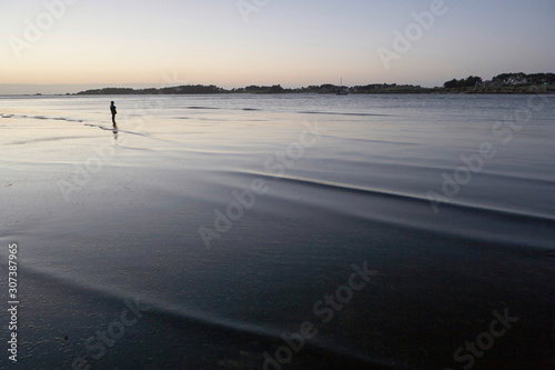 Low tide at a beach in Brittany in the evening, boy standing  alone in the shallow water, looking at the sea, loneliness