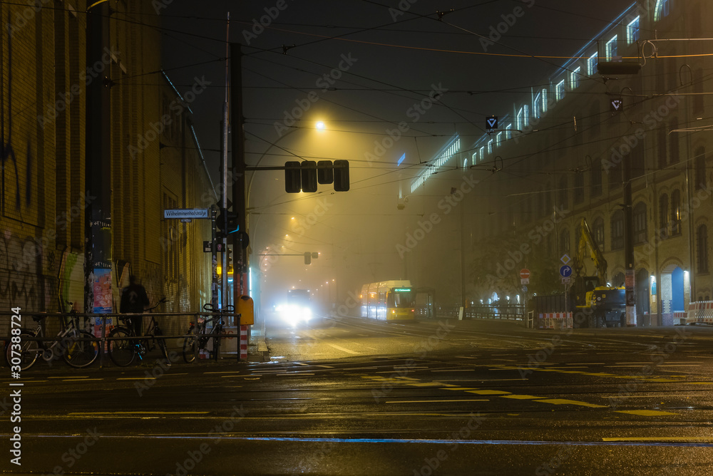 Naklejka premium Foggy Cross Road in a city at night, cross roads, wet and foggy cross road, traffic lights, tram station at night, foggy crossroad in Berlin Oberschöneweide