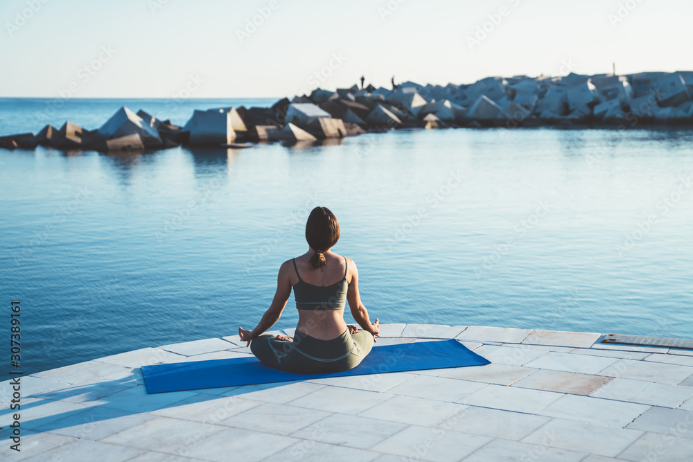 Anonymous female meditating in lotus position on stone pier