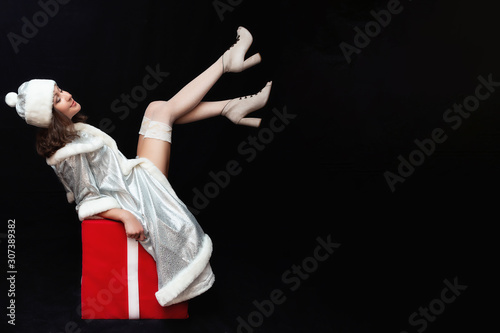 Sexy brunette girl in a snow maiden costume sits on a red cube, feet up. Happy new year