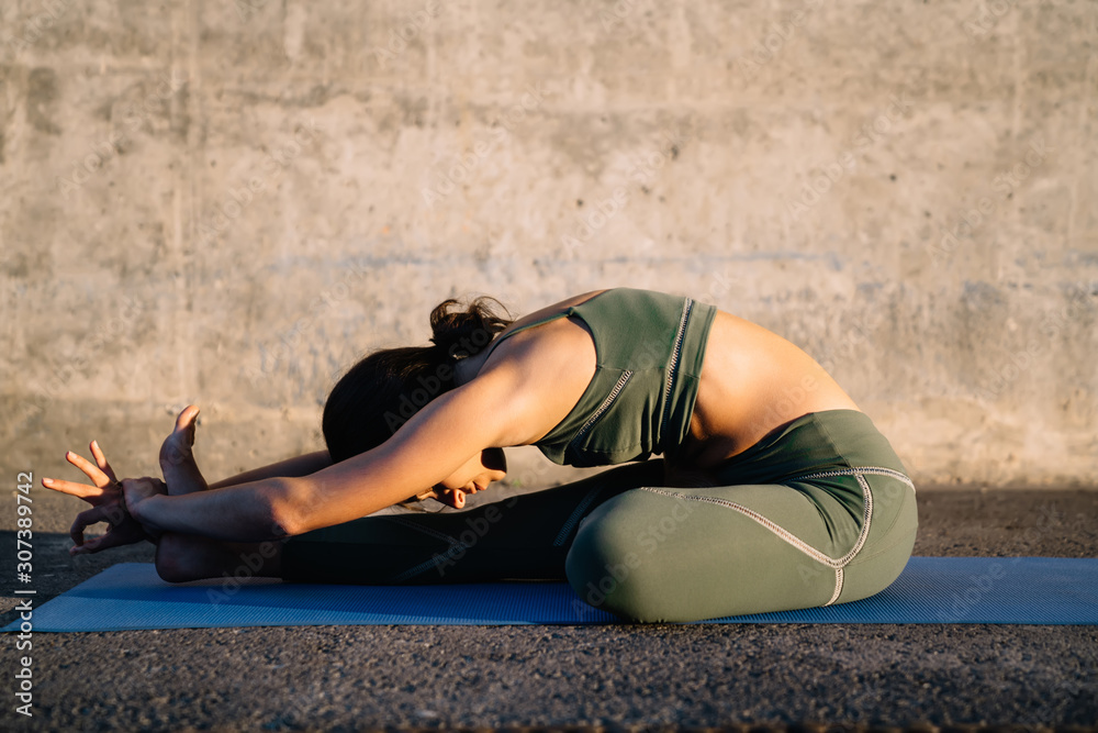 Young brunette making forward bend yoga pose against stone wall