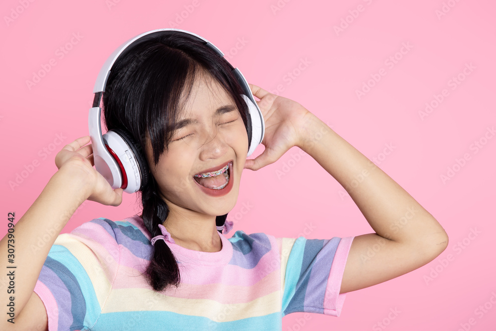Happy Asian teenager girl using headphone on pink background. Happy Asian teenager girl using headphone on pink background.
