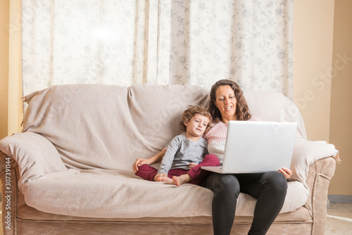 Child and woman sitting on a sofa watching a laptop.
