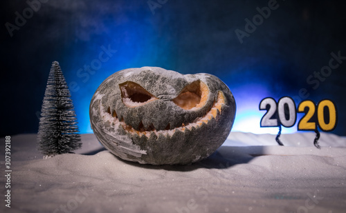 Christmas New Year or Halloween Celebrate Background with Little Christmas Tree on Blurred Bokeh Snow Background with horror pumpkin