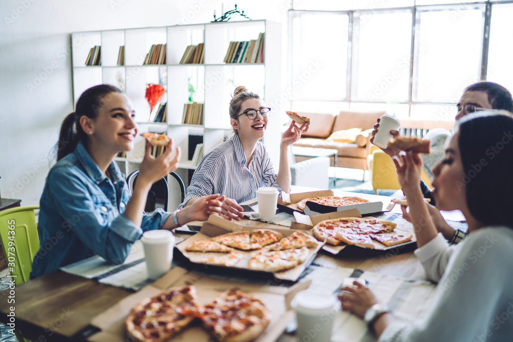 Smiling women eating pizza and speaking to friend at table