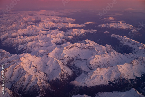 Stunning view of the snow covered Pyrénées in the south of France from the airplane window at sunset with a red pink glow