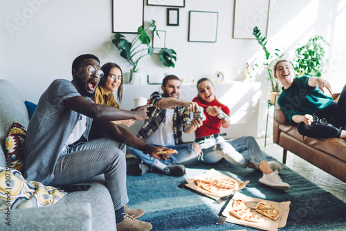 Astonished multiethnic adult people watching friends playing video game during home party