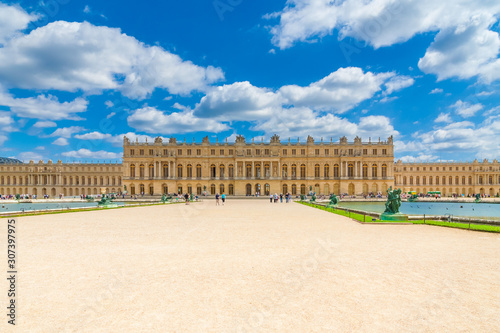 Beautiful panoramic view of the west facade of Versailles palace from the Water Parterre with two rectangular pools and a gravel path in the centre on a nice summer day with a blue sky.