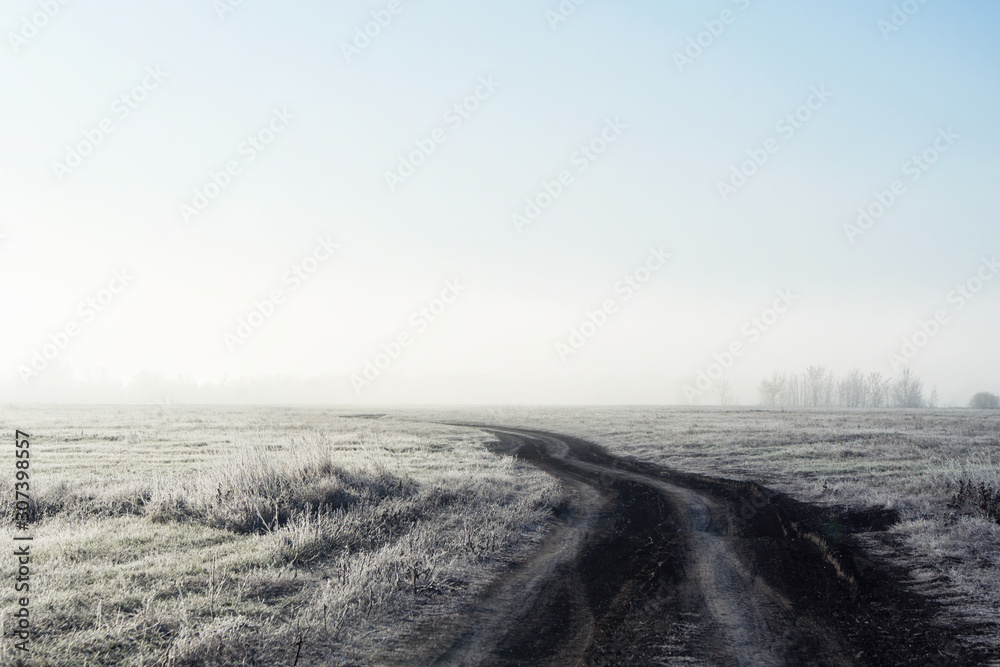 The road in dense fog through the field early winter morning. Selective focus, shallow depth of field.
