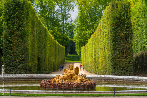 Gorgeous view of the Saturn Fountain, an allegory of Winter, with an alley of tall geometrical formed topiaries in the background in the Gardens of Versailles. It shows Saturn surrounded by putti. photo