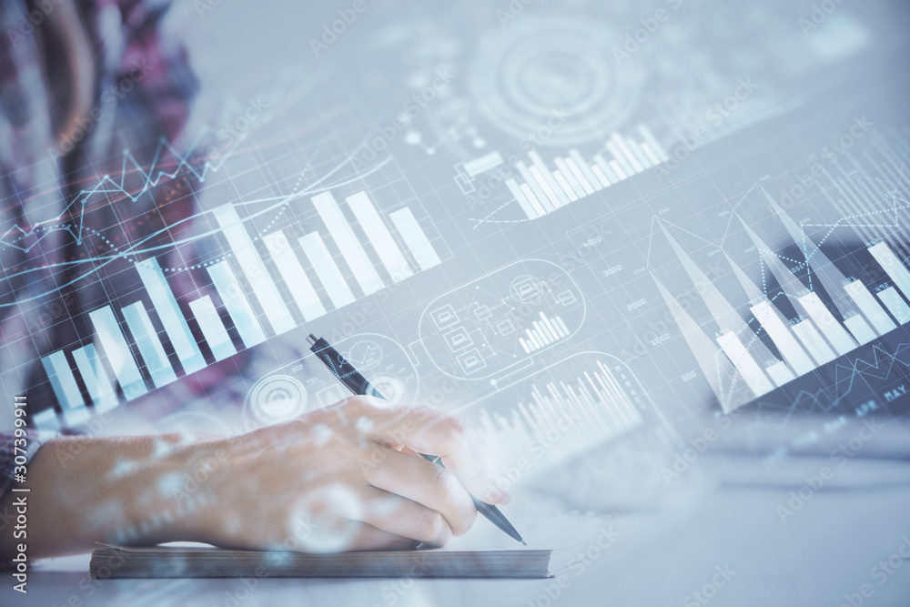 A woman hands writing information about stock market in notepad. Forex chart holograms in front. Concept of research. Double exposure A woman hands writing information about stock market in notepad. Forex chart holograms in front. Concept of research. Double exposure