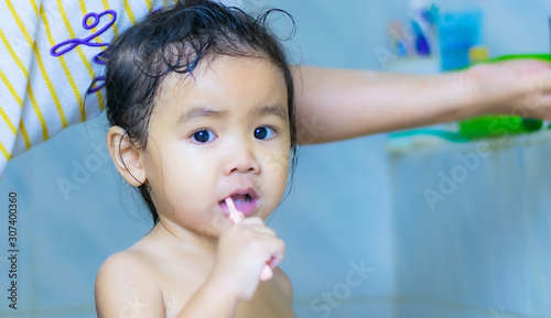 A young, 3 year old Asian woman is brushing her teeth in the bathroom.