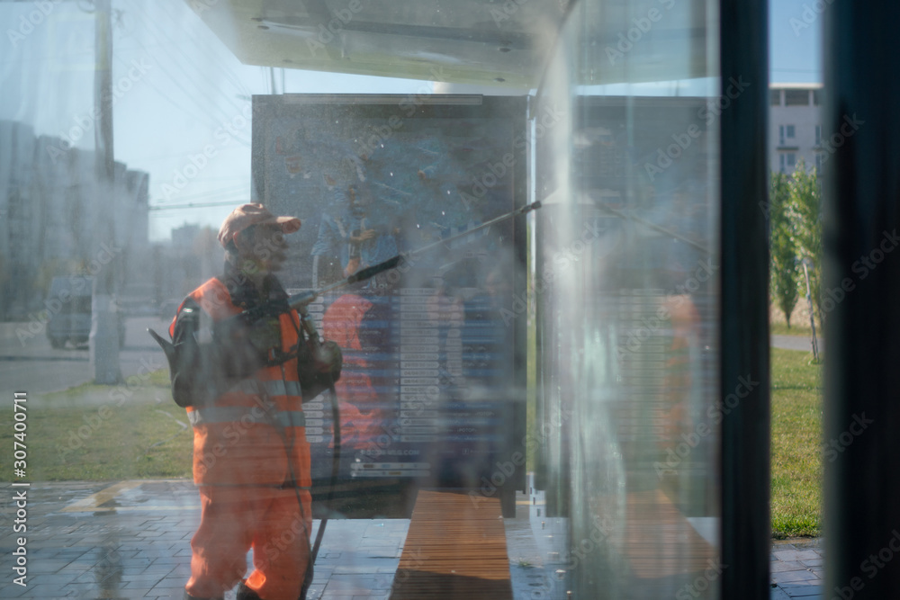Φωτογραφία the city cleaning service man in orange uniform washing the bus stop glass with