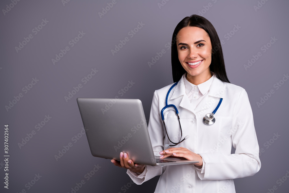 Portrait of beautiful experienced woman medic specialist hold computer she use consult patient search prescription wear white coat stethoscope isolated over grey color background Portrait of beautiful experienced woman medic specialist hold computer she use consult patient search prescription wear white coat stethoscope isolated over grey color background