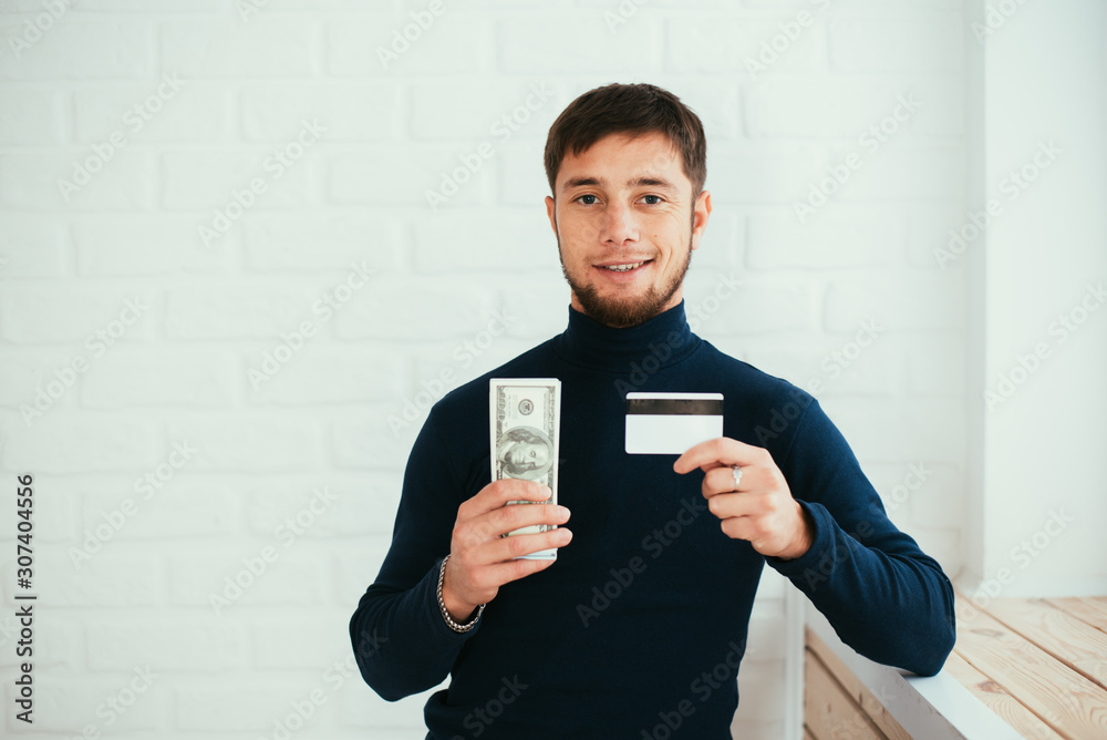 A man with a credit card and money in his hands happy on a brick white background A man with a credit card and money in his hands happy on a brick white background