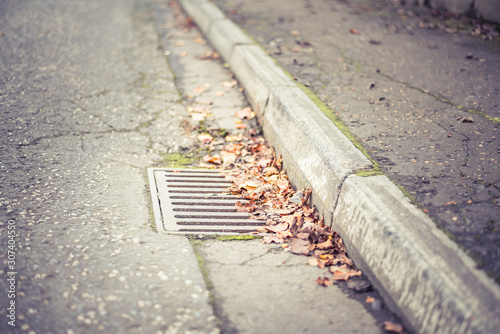 Flooding threat, fall leaves clogging a storm drain on a wet day, street and curb
