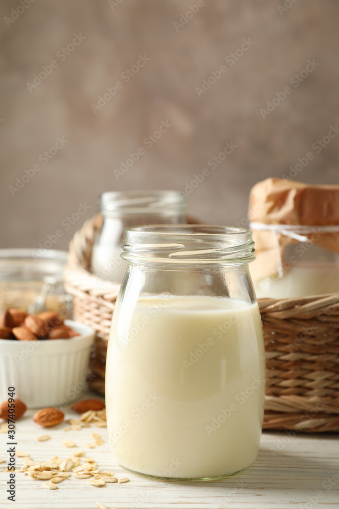 Bottle of oat milk, basket with a glasses of different types milk on wooden background, space for text