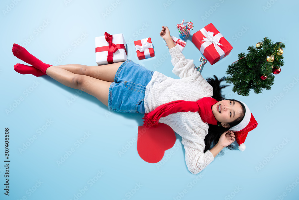 Asian teenager girl wearing Santa hat lying on floor with red heart shape speeh bubble and Christmas tree and gift boxes.