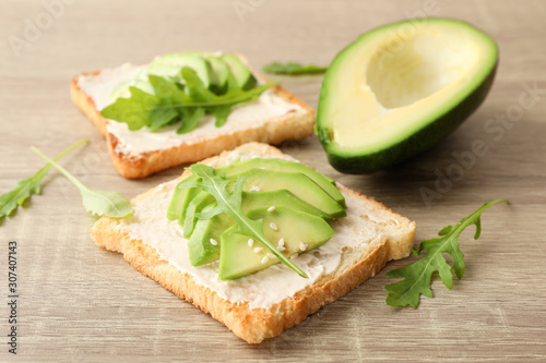 Toasts with butter, avocado, arugula and sesame on wooden background, close up