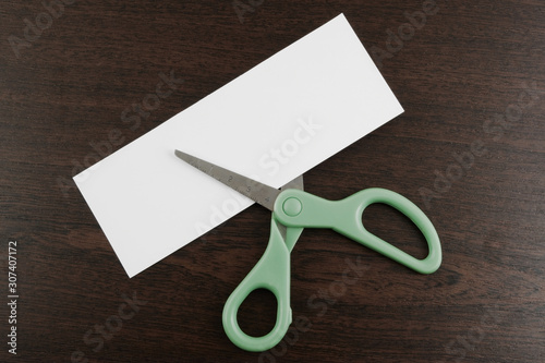 Scissors cutting blank paper card for text on table background photo