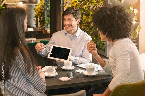Excited man showing blank tablet to his colleagues in cafe