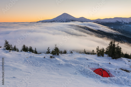Winter camping high in the mountains, among the clouds and fog in the red tourist tent.