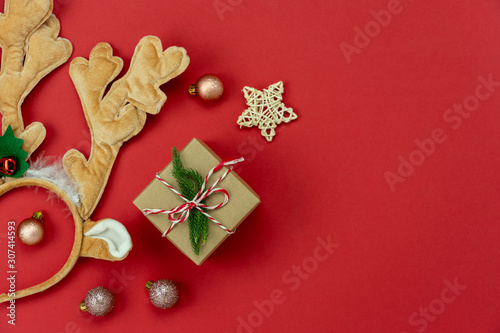 Table top view of Merry Christmas decorations & Happy new year ornaments concept.Flat lay essential difference objects gift box & fir tree on modern red paper background at home studio office desk.