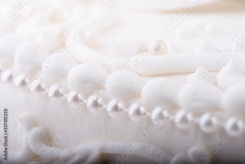 White Wedding cake detail closeup with fondant, swirls, and decorative pearls