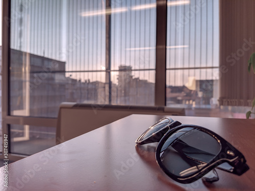 Retro old style sunglasses placed on wooden desk at a office work with big windows in the background with beautiful sunny weather outside