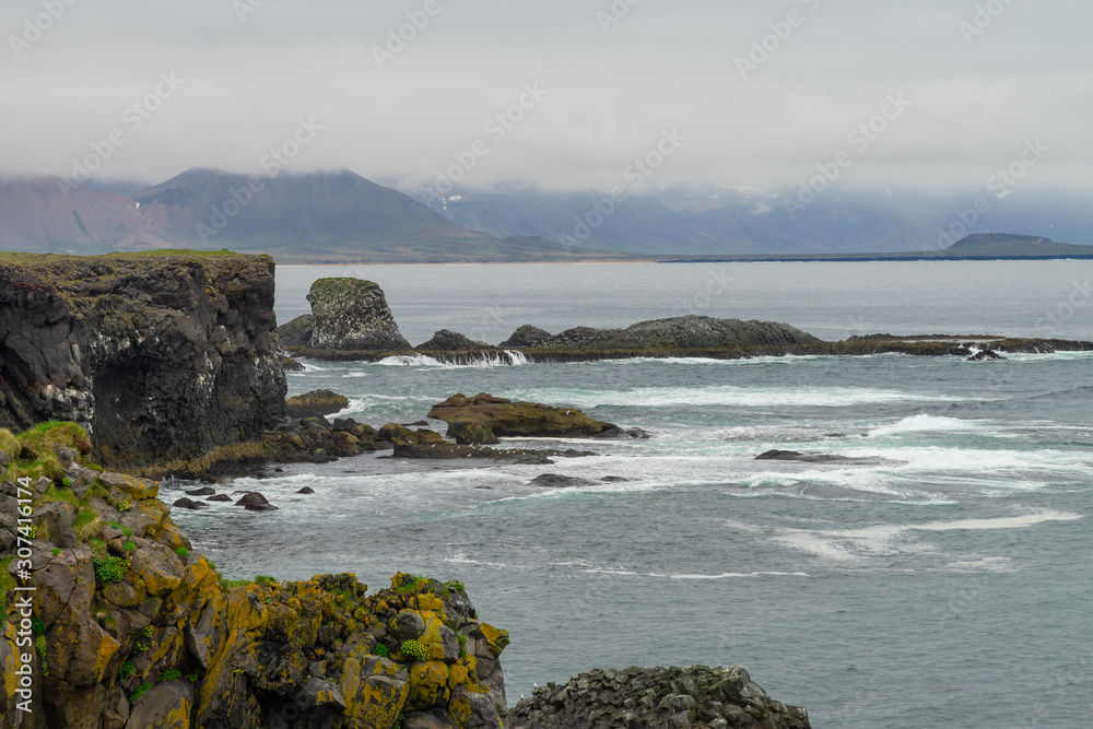 the ocean around the island. Volcanic rock is washed with water. The Country Of Iceland. A high cliff into the clear blue water.